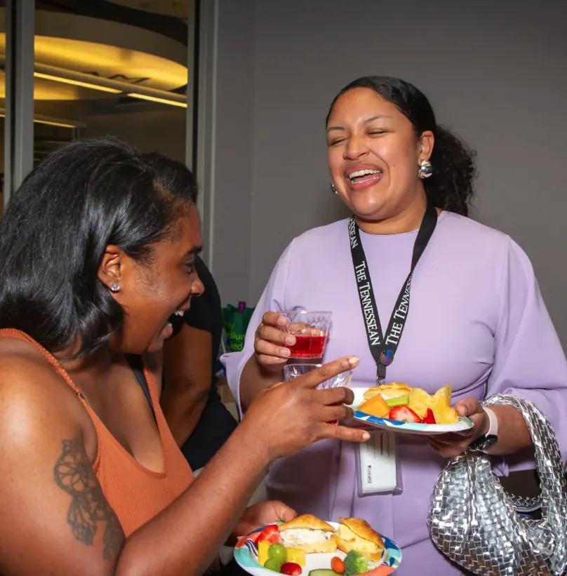 Women laughing together at an event, one in a lavender dress