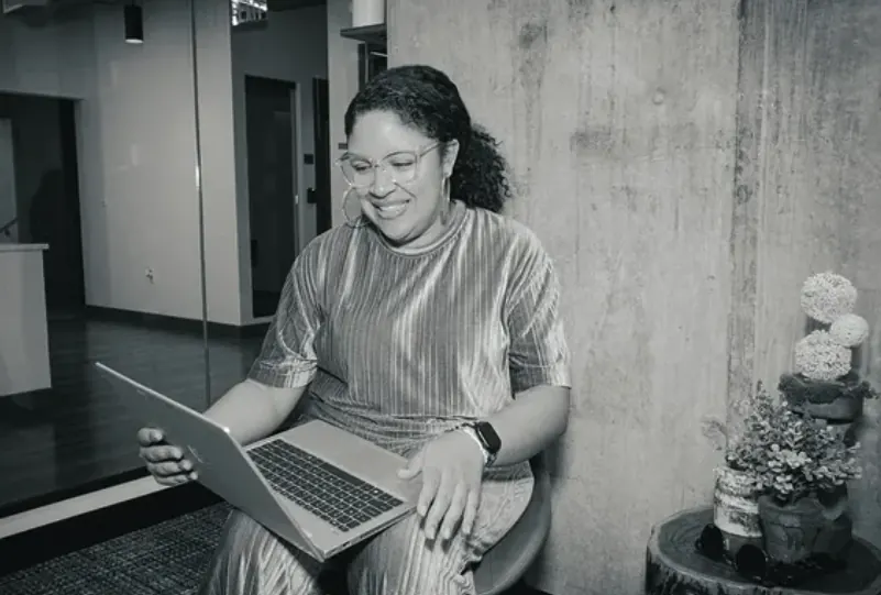 A woman smiling at her laptop, black and white