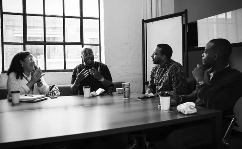 Four people in conversation around a meeting table, black and white